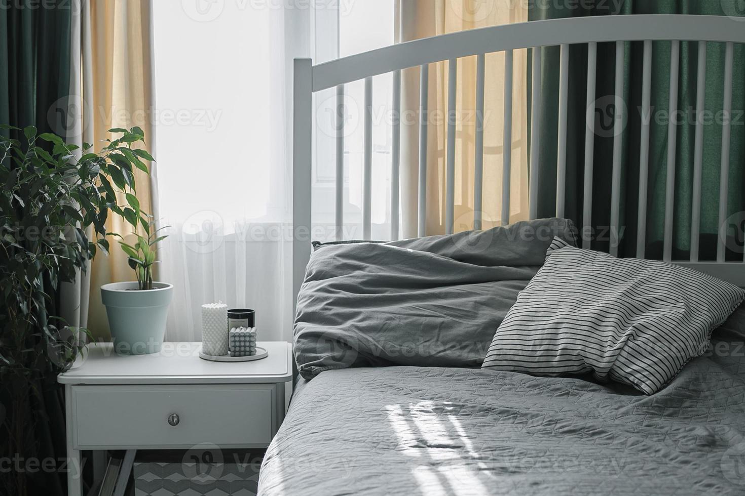 Schlafzimmer mit hellem Interieur. Moderne Kerze, heimische Pflanze auf dem Nachttisch neben dem Bett. Lebensstil zu Hause foto