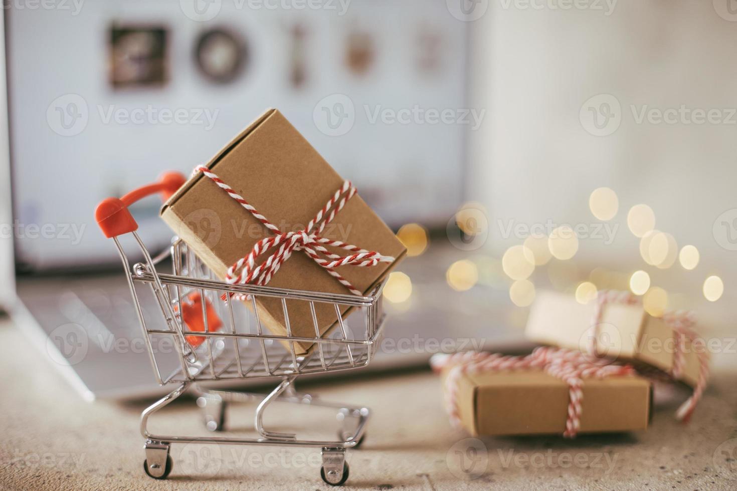 Mini-Einkaufswagen mit Geschenkbox auf dem Schreibtisch in der Nähe des Laptops. Konzept des Online-Shoppings. foto