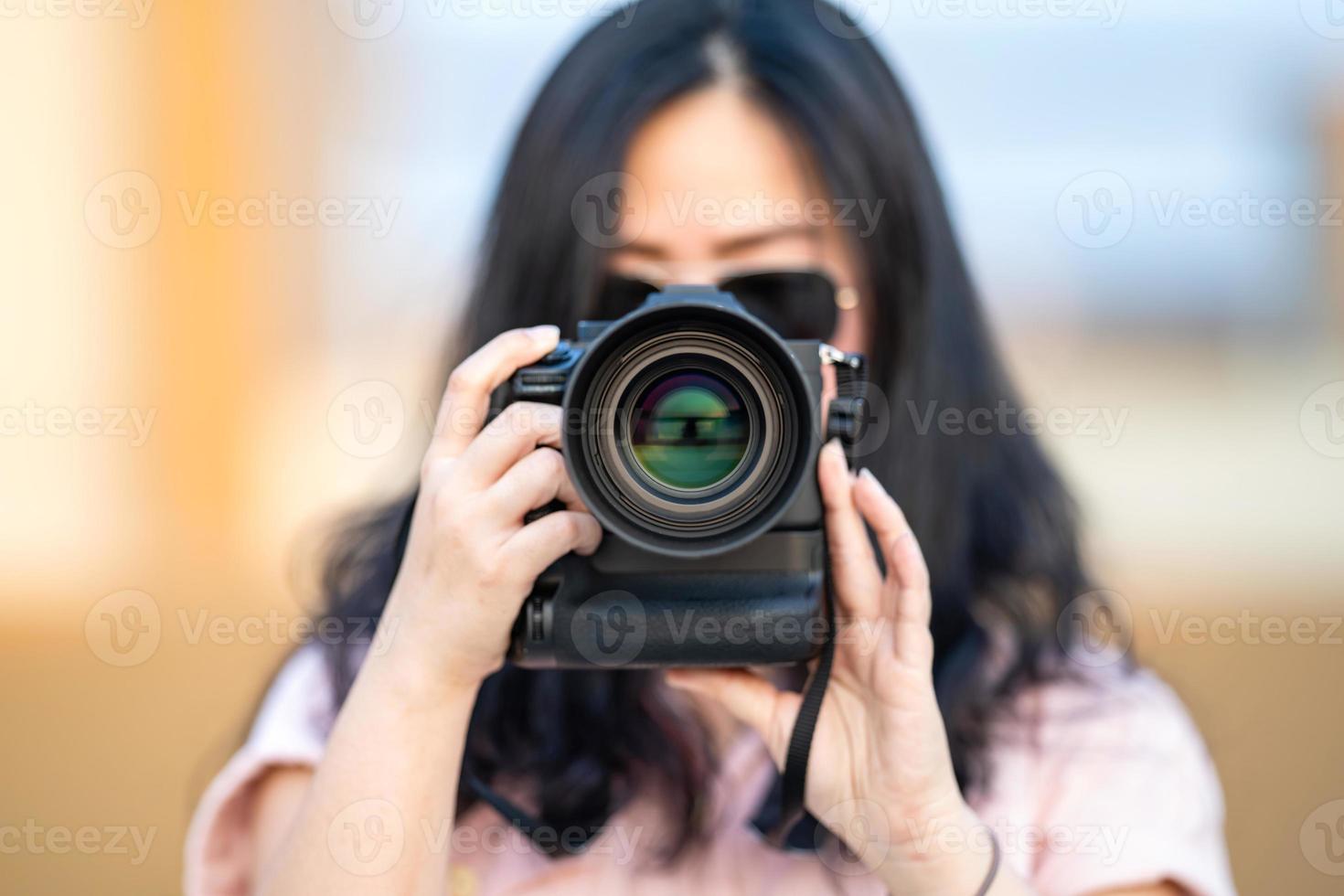 Amateur-Sonnenbrille asiatische Frau macht ein Foto mit einer professionellen spiegellosen Kamera im blauen Dachgebäude im Freien in der Dämmerungszeit.