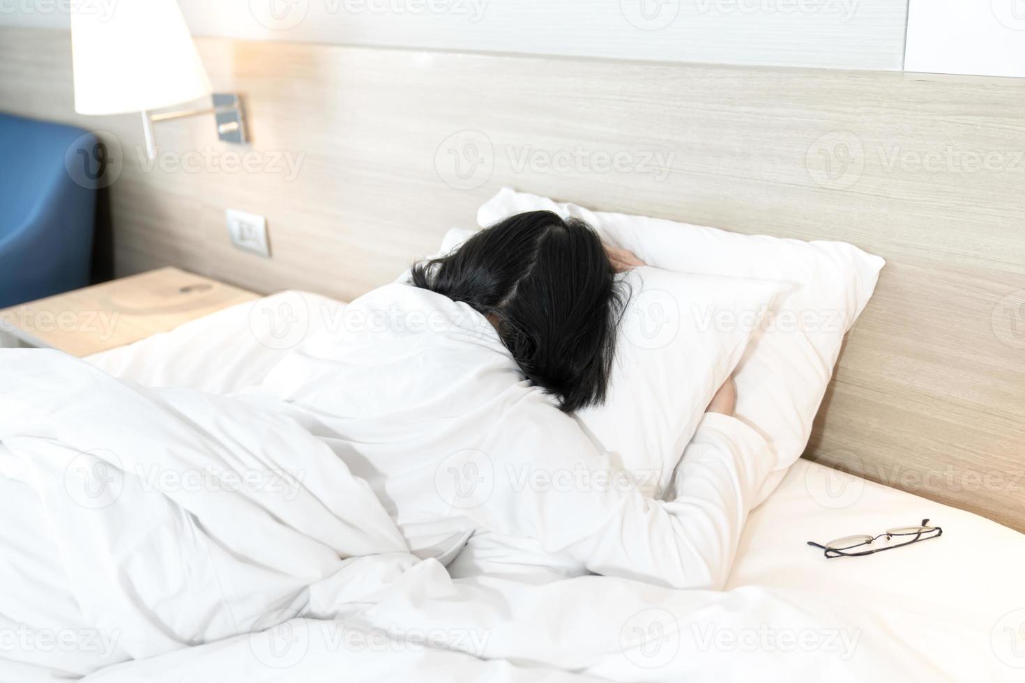 asiatische dame im weißen langarm-t-shirt-pyjama liegt auf dem bauch im bett mit erschöpfter stimmung und ton. foto