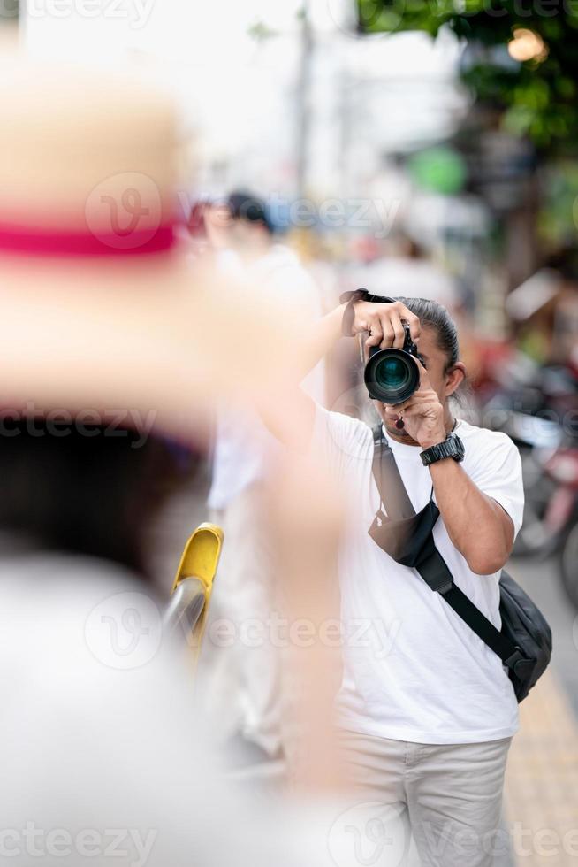 Professioneller asiatischer Kameramann konzentriert sich mit seiner spiegellosen Kamera neben dem Straßenfeld auf das Bild. foto