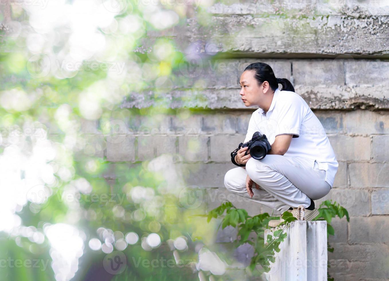 asiatischer professioneller kameramann sitzt und denkt darüber nach, wie man ein kreativitätsfoto im hintergrund und in der umgebung des baubereichs erstellt. foto