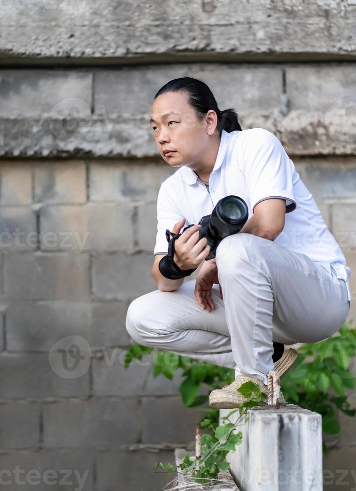 asiatischer professioneller kameramann sitzt und denkt darüber nach, wie man ein kreativitätsfoto im hintergrund und in der umgebung des baubereichs erstellt. foto