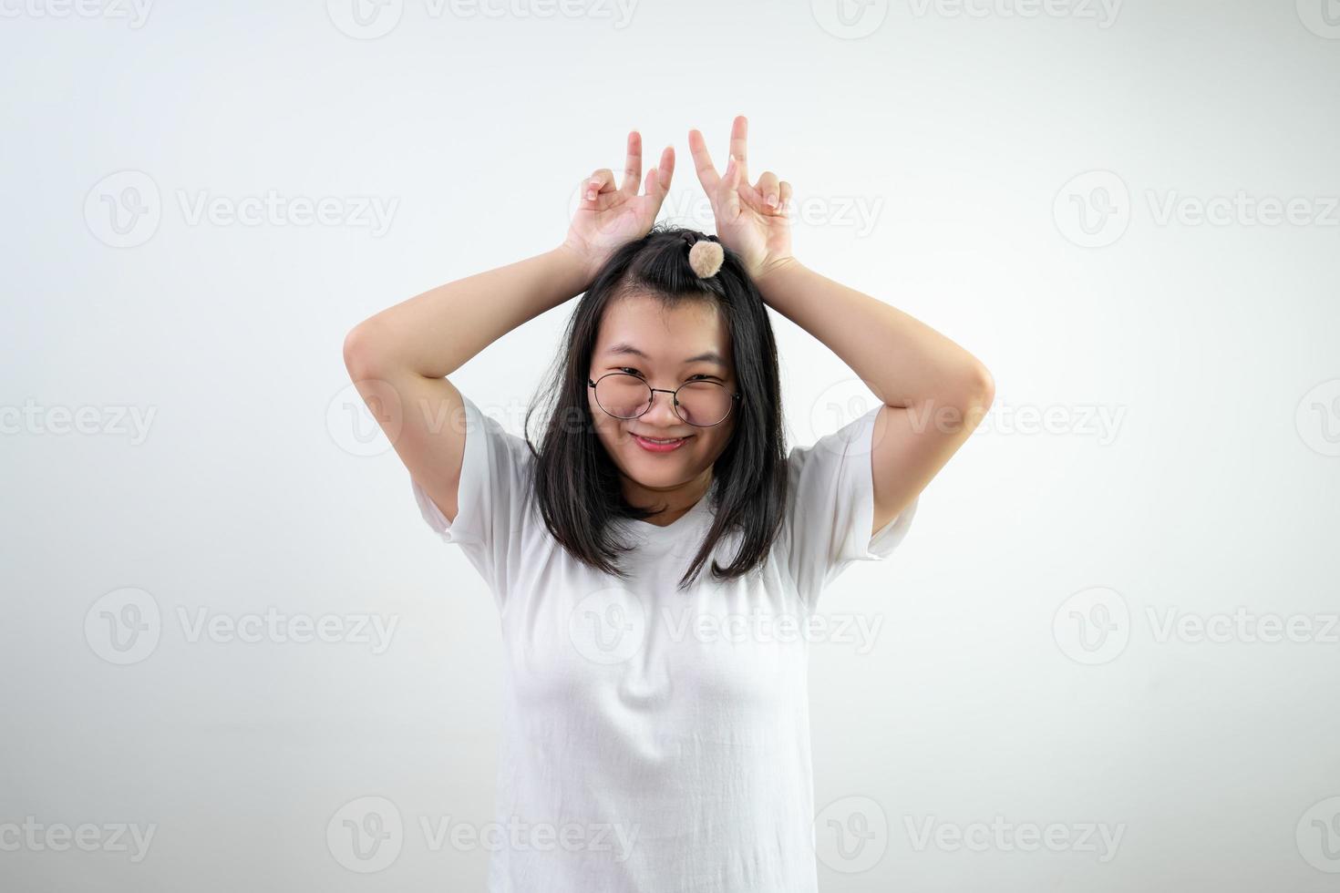 asiatische Brille junge Frau hebt Victory-Zeichen mit zwei Fingern wie die Hasenohren auf weißem Hintergrund. foto