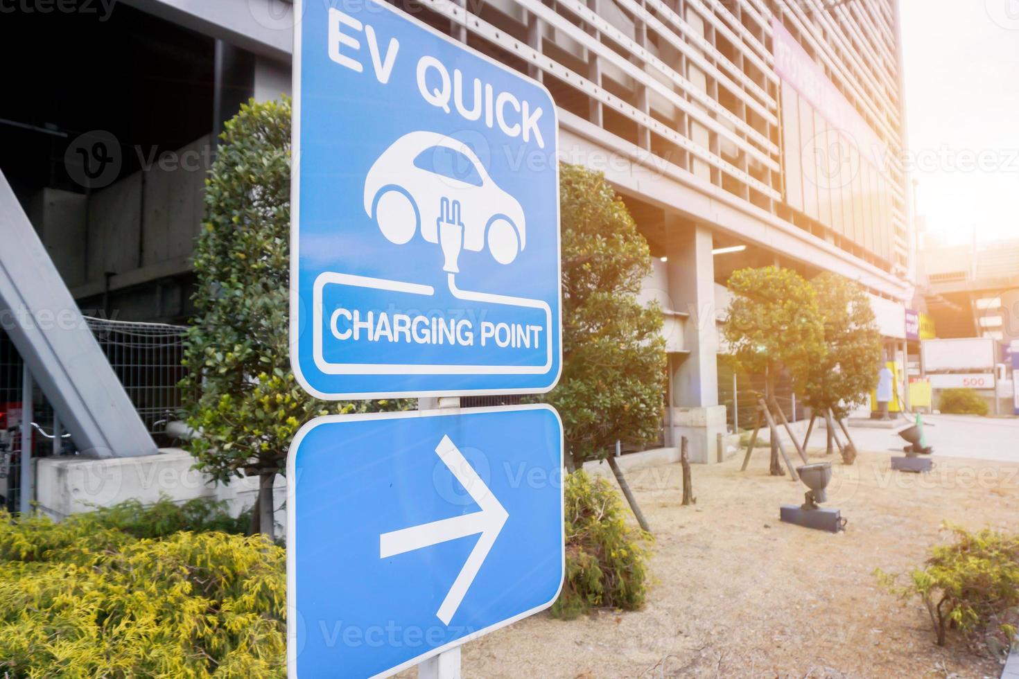 Perspektivische Ansicht und Nahaufnahme Zeichen und Symbol der Ladestation für Elektroautos mit Navigationspfeil auf verschwommenem Gebäude und Sonneneruptionshintergrund. foto