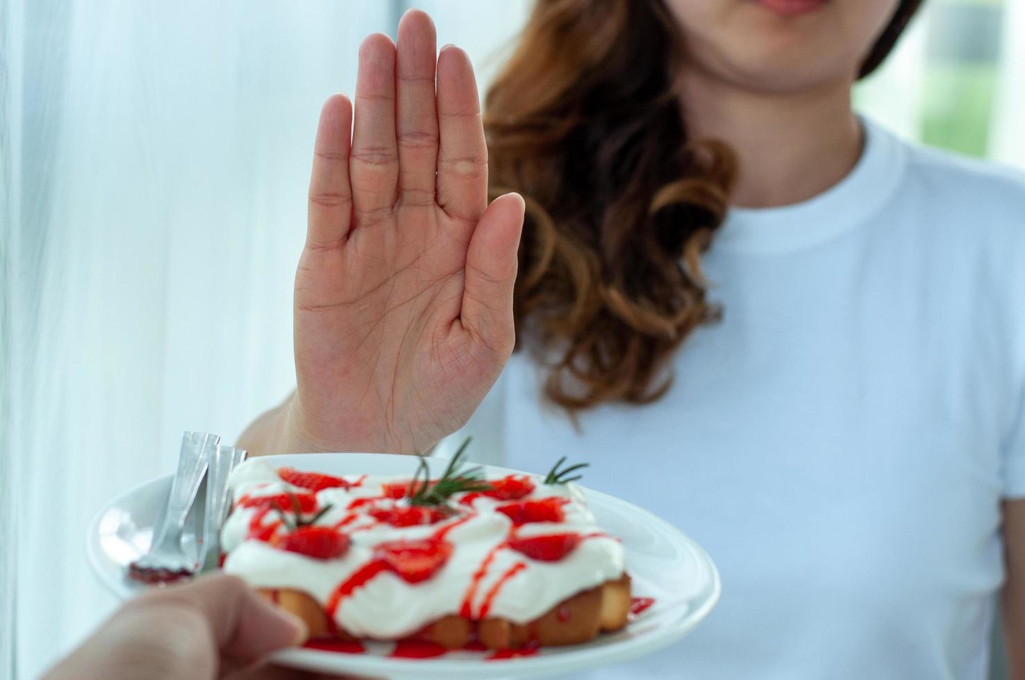 Junge Frau benutzt die Hand, um den Teller mit Gebäck zu schieben, weigert sich, Mehl und Zucker zu essen, um Gewicht zu verlieren. foto