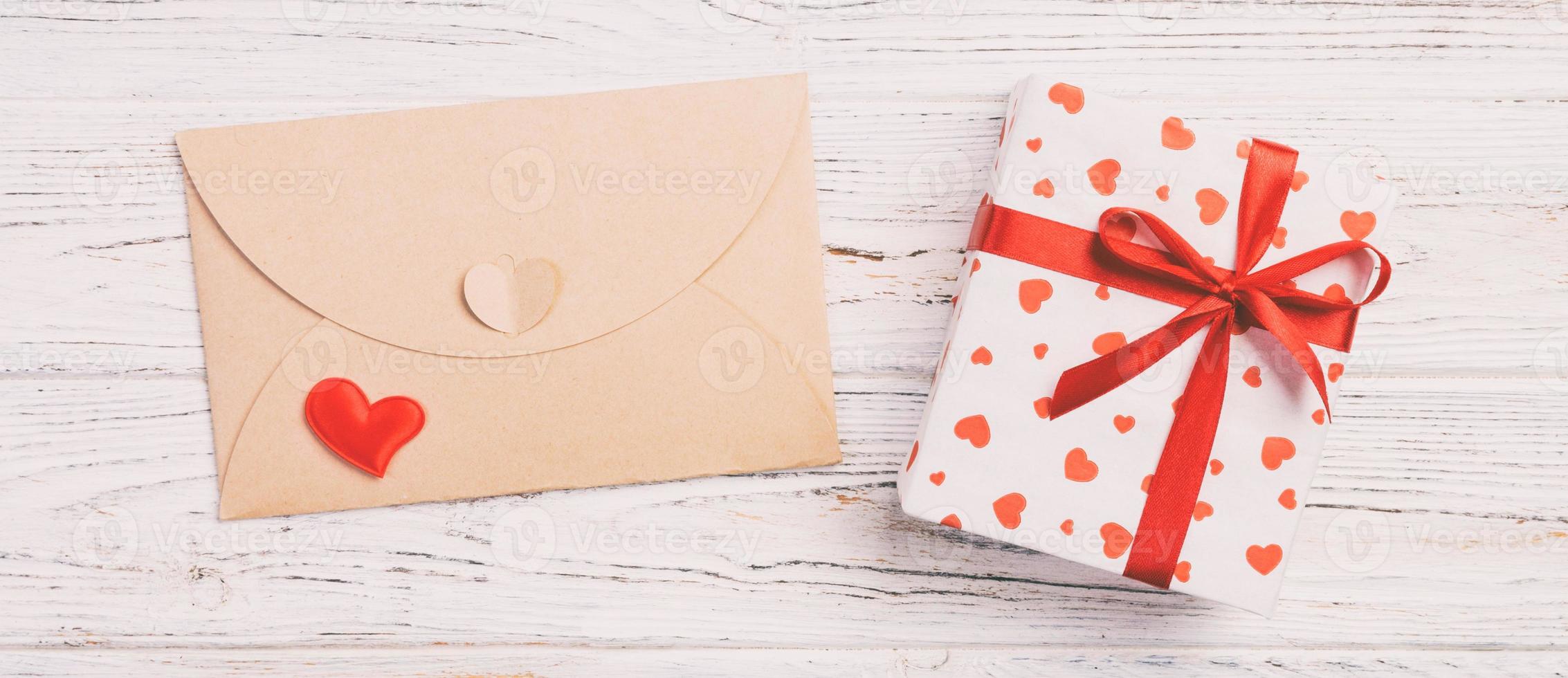 Briefumschlag mit rotem Herzen und Geschenkbox auf weißem Holzhintergrund. valentinstagkarte, liebes- oder hochzeitsgrußkonzept foto
