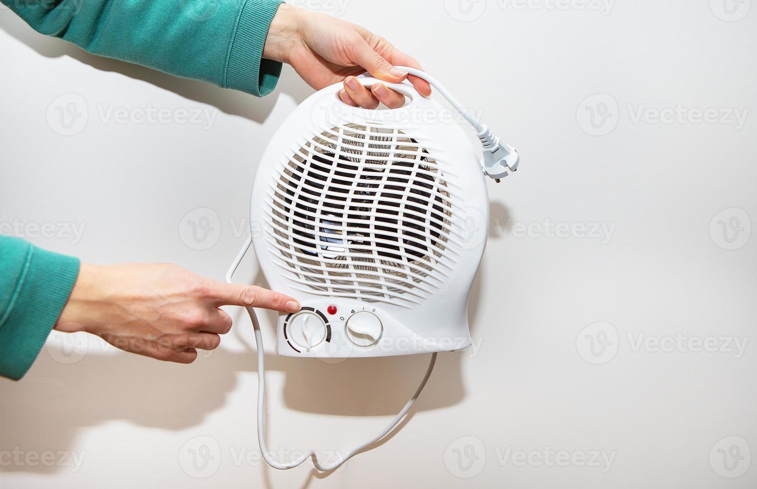 Heizung isoliert auf weißem Hintergrund. Ein Mädchen hält einen Heizlüfter aus Kunststoff und zeigt den Temperaturregler. foto