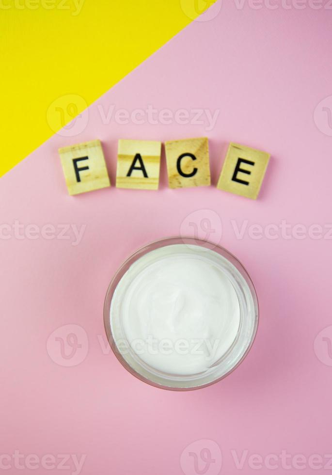 feuchtigkeitsspendende kosmetische creme in einem glastopf, auf gelb-rosa hintergrund, holzbuchstaben stehen auf dem tisch. foto