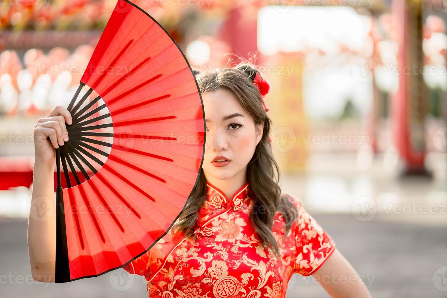 Frohes chinesisches Neujahrsfest. junge dame, die traditionelles cheongsam qipao kostüm trägt, das fan im chinesischen buddhistischen tempel hält. foto