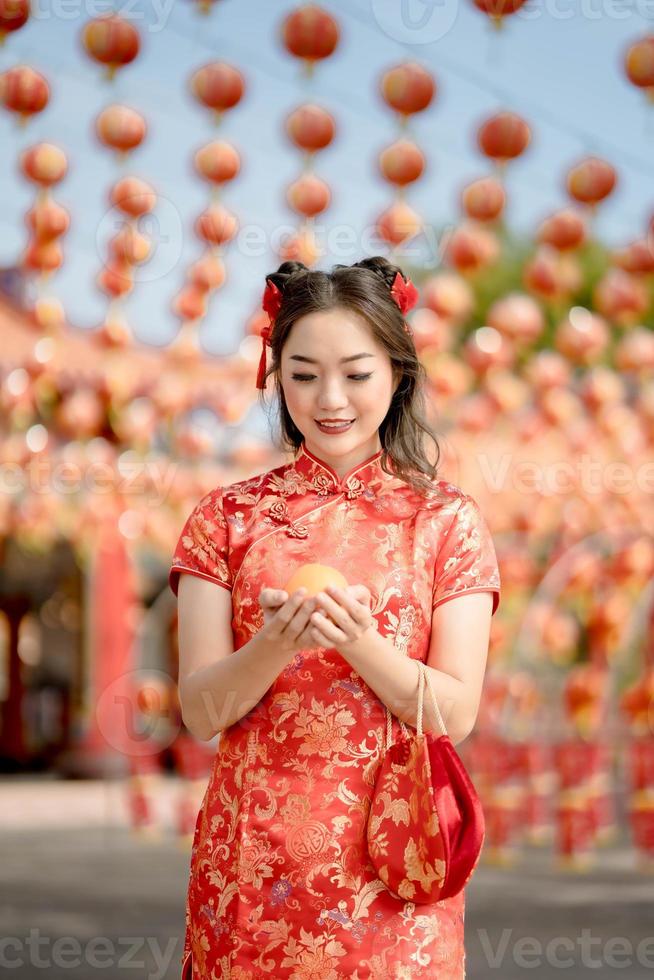 frohes chinesisches neujahr. eine junge dame, die traditionelles cheongsam qipao kleid trägt, das altes goldgeld und tasche im chinesischen buddhistischen tempel hält. Feiern Sie das chinesische Neujahrsfest, die Feiertage der festlichen Jahreszeit. foto