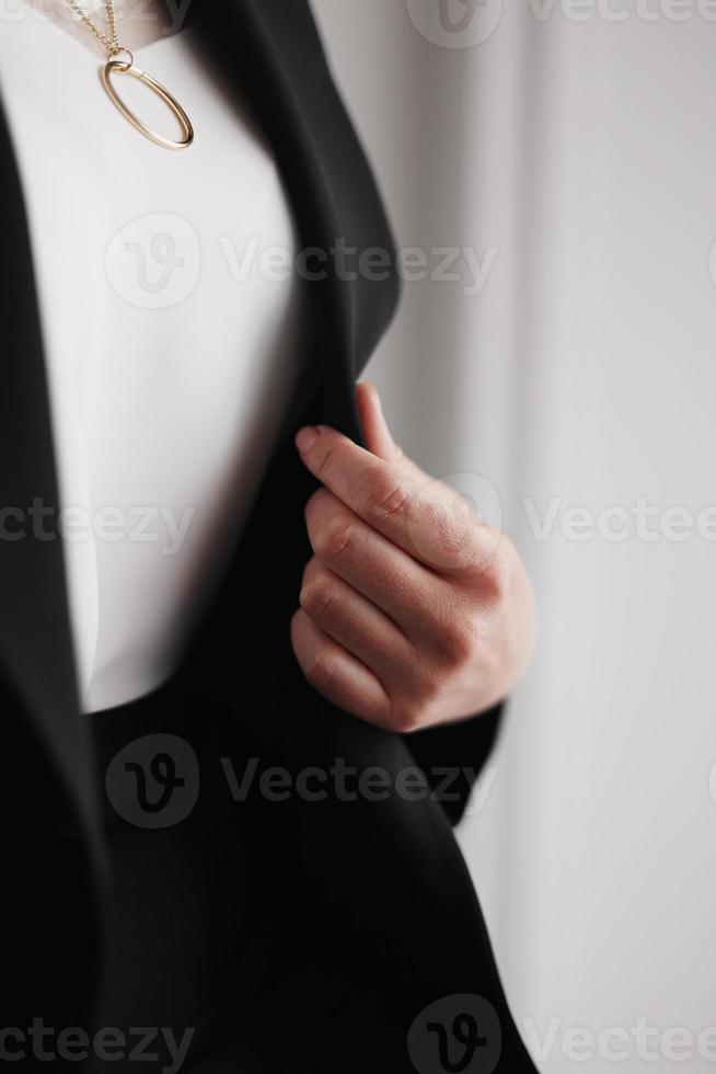 stilvolle goldene Kette mit Kreis am Hals einer Frau. Frau in schwarzer Jacke und weißer Bluse, beschnittene Ansicht. elegantes Accessoire foto