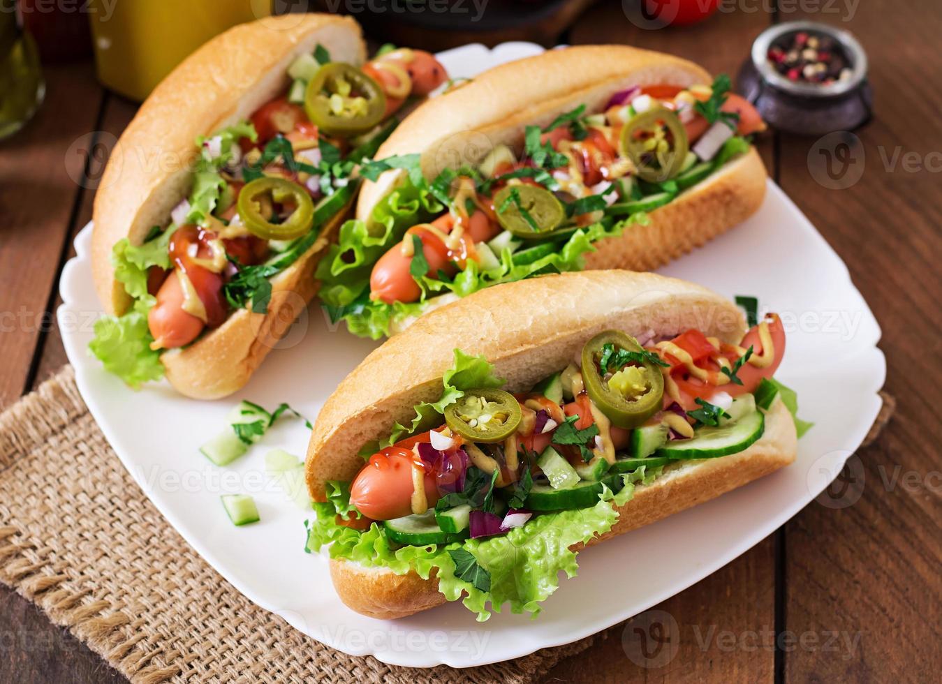 Hot Dog mit Jalapenopfeffer, Tomaten, Gurken und Salat auf Holzhintergrund foto