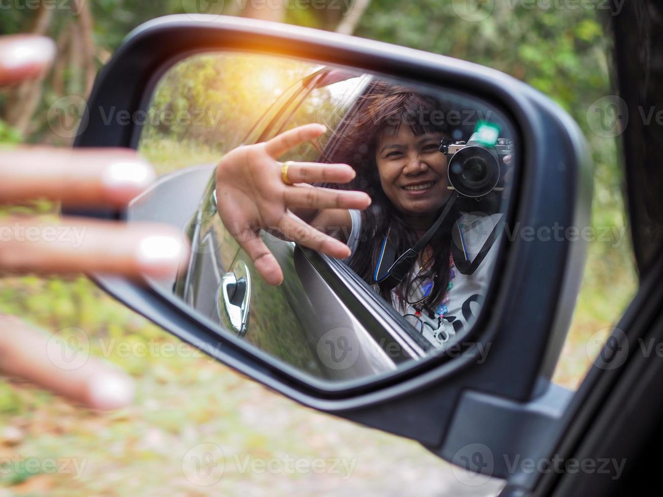 Eine Frau hält eine Digitalkamera und fotografiert sich lächelnd im Autospiegel. foto