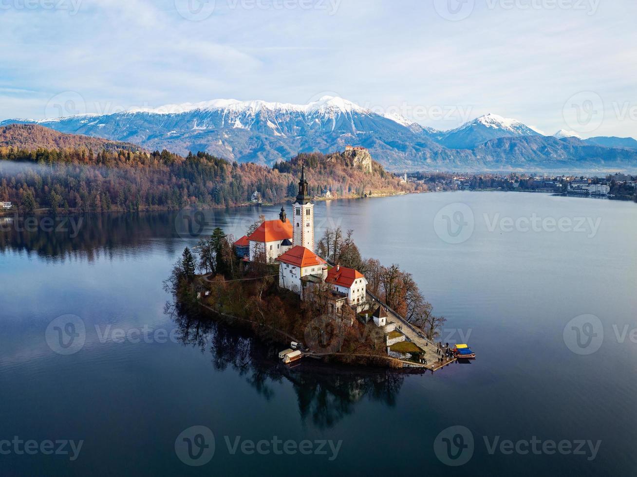 luftdrohnenansicht der sonnenaufgangswinterlandschaft des magischen sees bled in slowenien. ein Wintermärchen für romantische Erlebnisse. Berge mit Schnee im Hintergrund. Kirche der Gottesmutter im See. foto