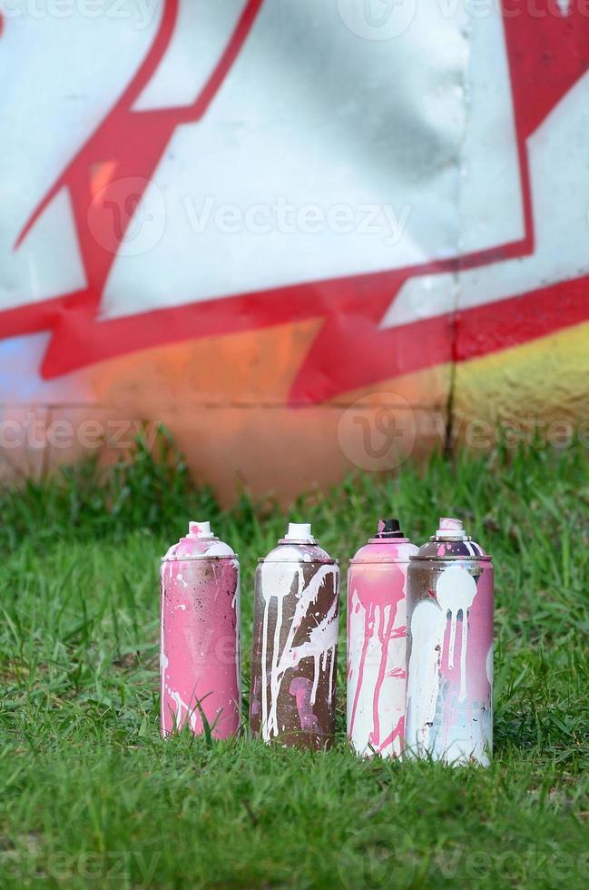 Ein paar gebrauchte Farbdosen liegen auf dem Boden in der Nähe der Wand mit einem schönen Graffiti-Gemälde. Straßenkunst- und Vandalismuskonzept foto