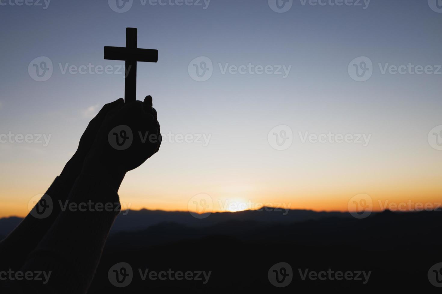 Silhouette aus Händen, die Holzkreuz auf Sonnenaufgangshintergrund, Kruzifix, Symbol des Glaubens halten. foto