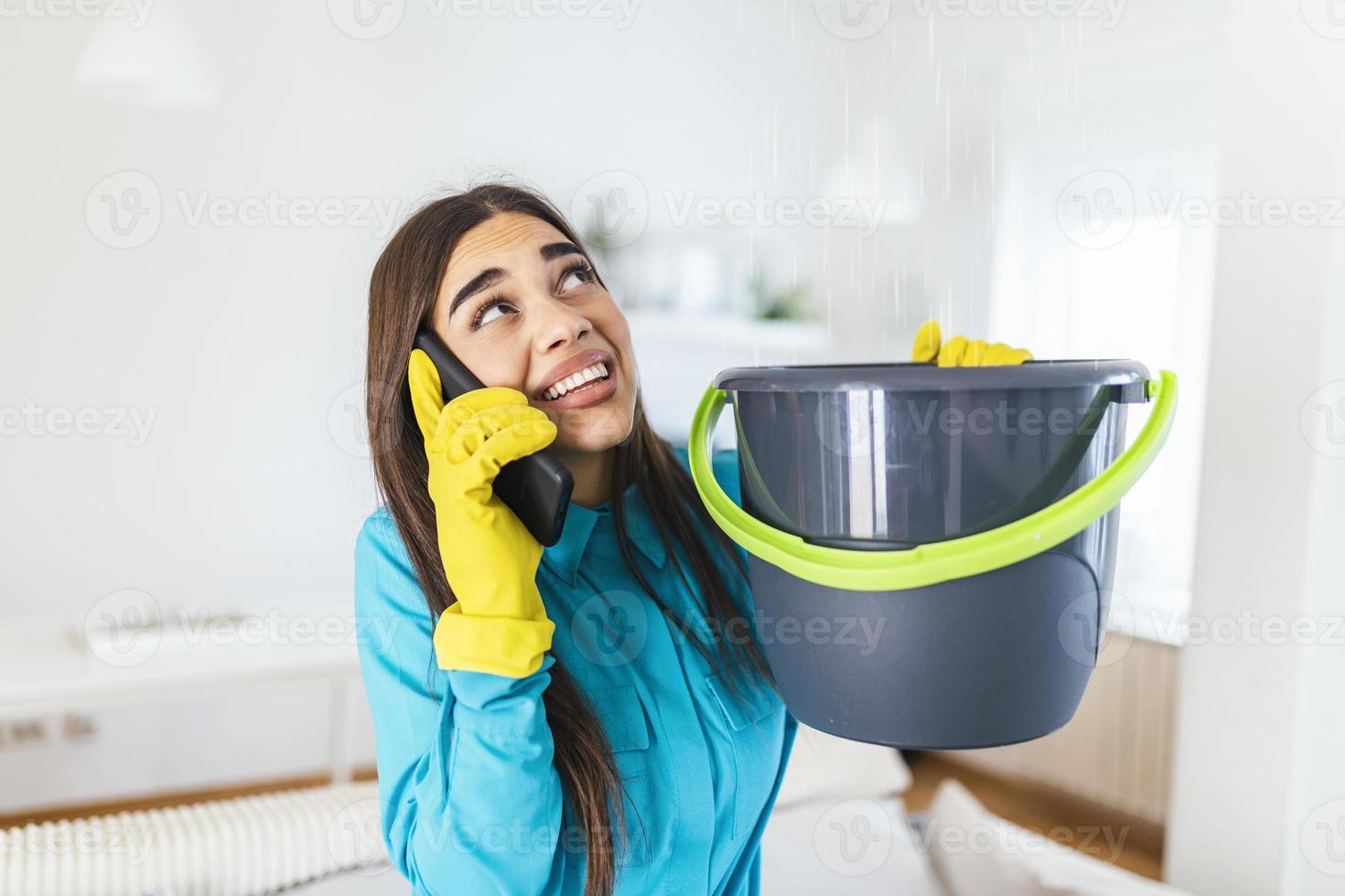 schockierte frau, die klempner anruft, während sie mit utensilien aus der decke austretendes wasser sammelt foto