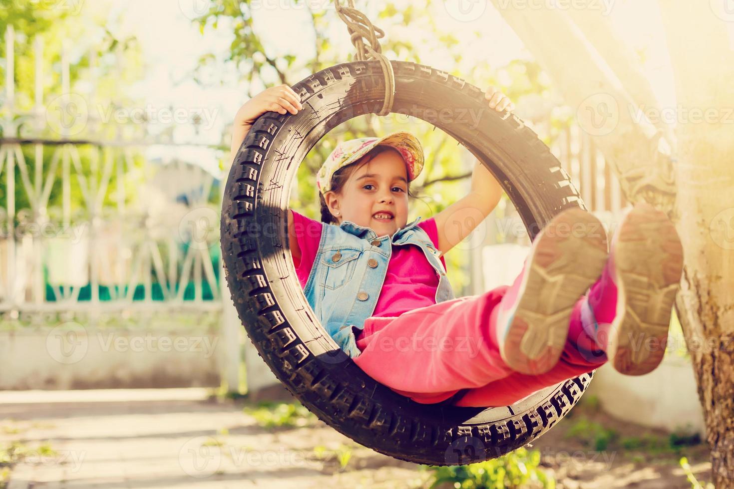 glückliches kleines mädchen, das swing im park spielt, gefilterte töne foto