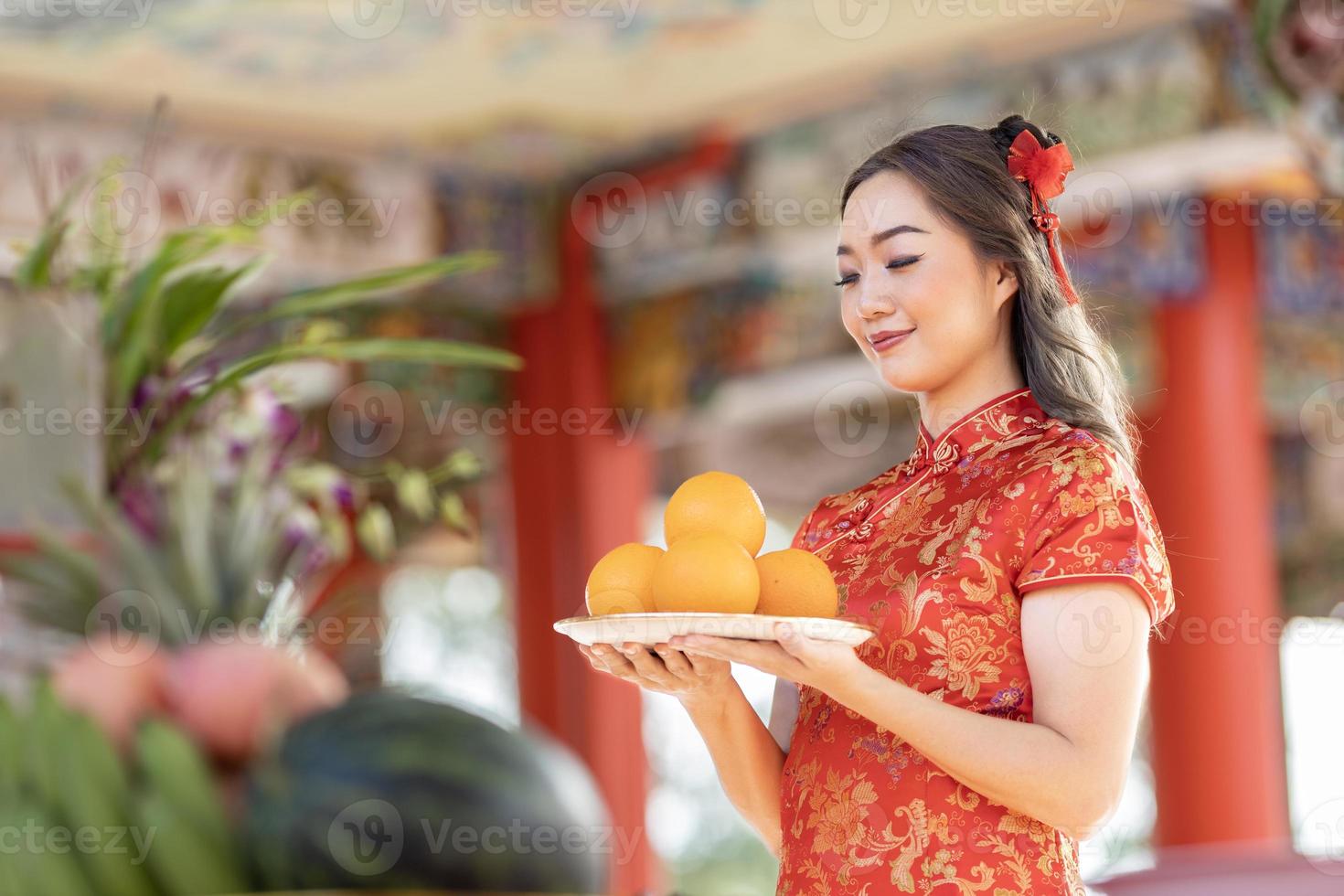 asiatische frau im roten cheongsam qipao kleid bietet dem angestammten gott im chinesischen buddhistischen tempel während des neuen mondjahres für den besten wunschsegen und das vielglückkonzept eine mandarine an foto