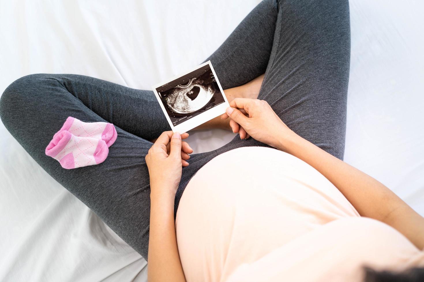 Eine schwangere Frau betrachtet ein Ultraschallfoto des Fötus. mutter berührt das baby sanft auf dem bauch. frauen sind 30 wochen schwanger. erste Liebe im Bauch und letzte Schwangerschaft foto