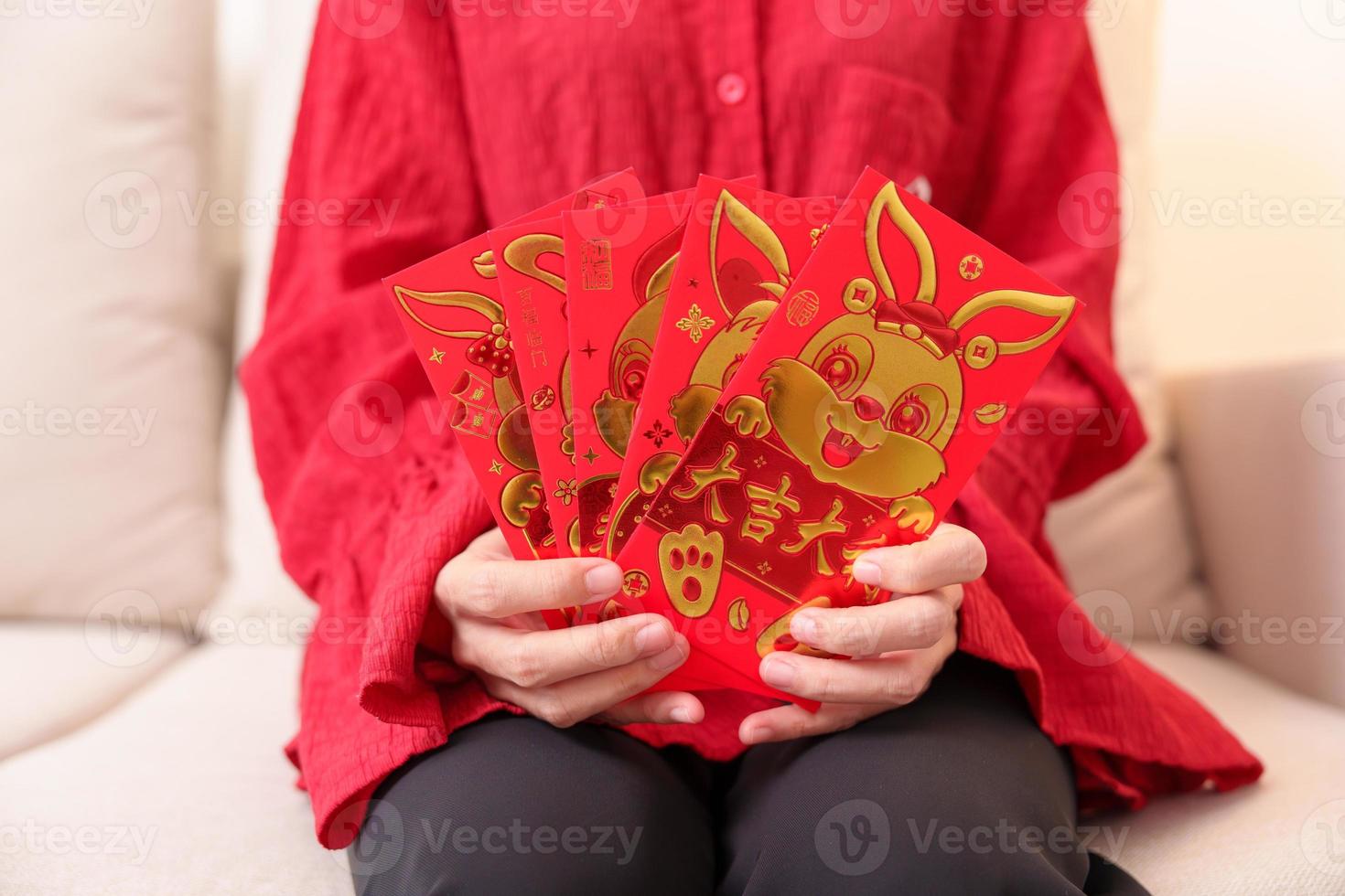 frau, die chinesischen roten umschlag mit goldenem kaninchen und segnungswort, geldgeschenk für glücklichen mondneujahrsfeiertag hält. Chinesischer Satz bedeutet Glück, gesund, glücklich und wohlhabend foto