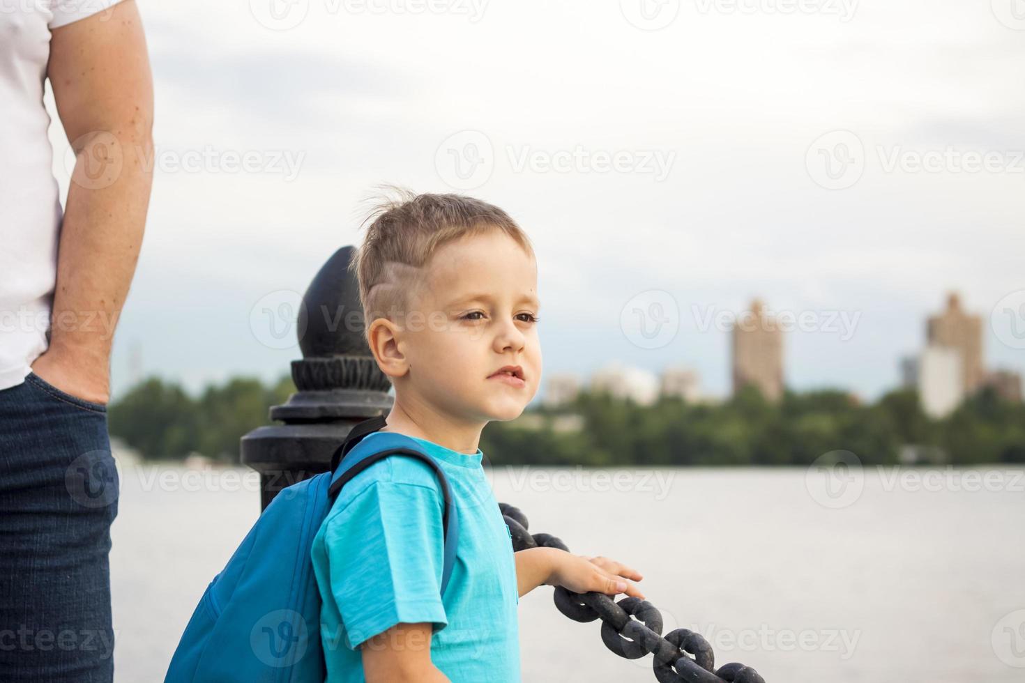 ein Junge in einem blauen T-Shirt mit einem Rucksack auf dem Rücken. Reise. Das Gesicht drückt natürliche freudige Emotionen aus. nicht inszenierte Fotos aus der Natur