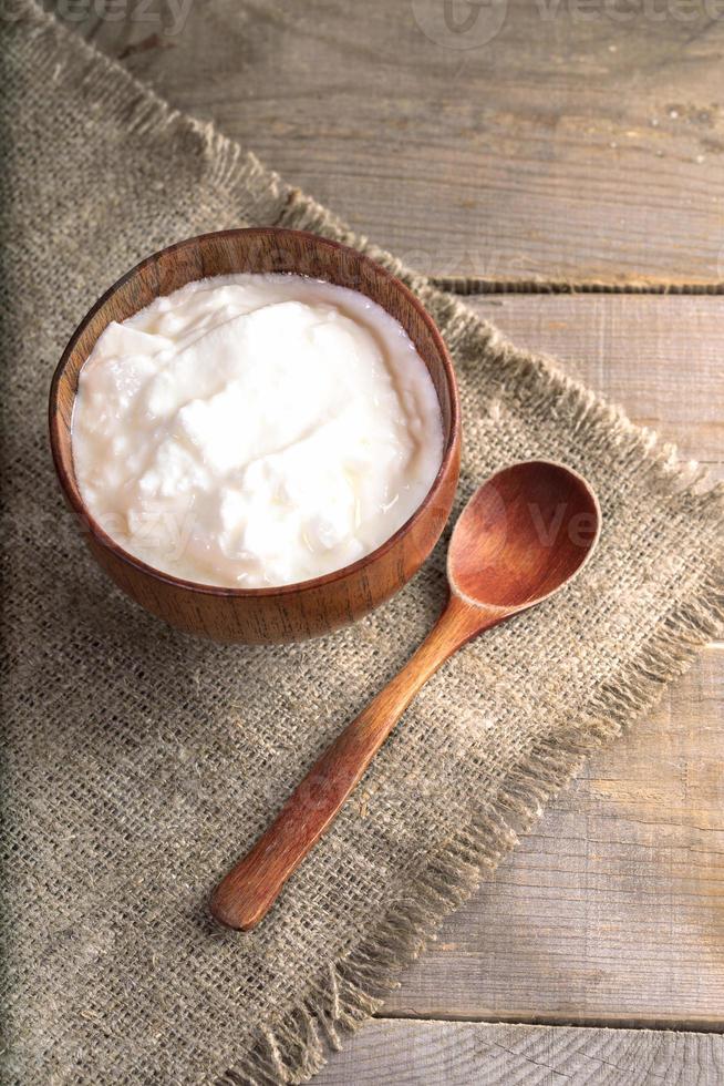 Joghurt in Holzschale mit Holzlöffel auf Sackleinen auf Holztisch. foto