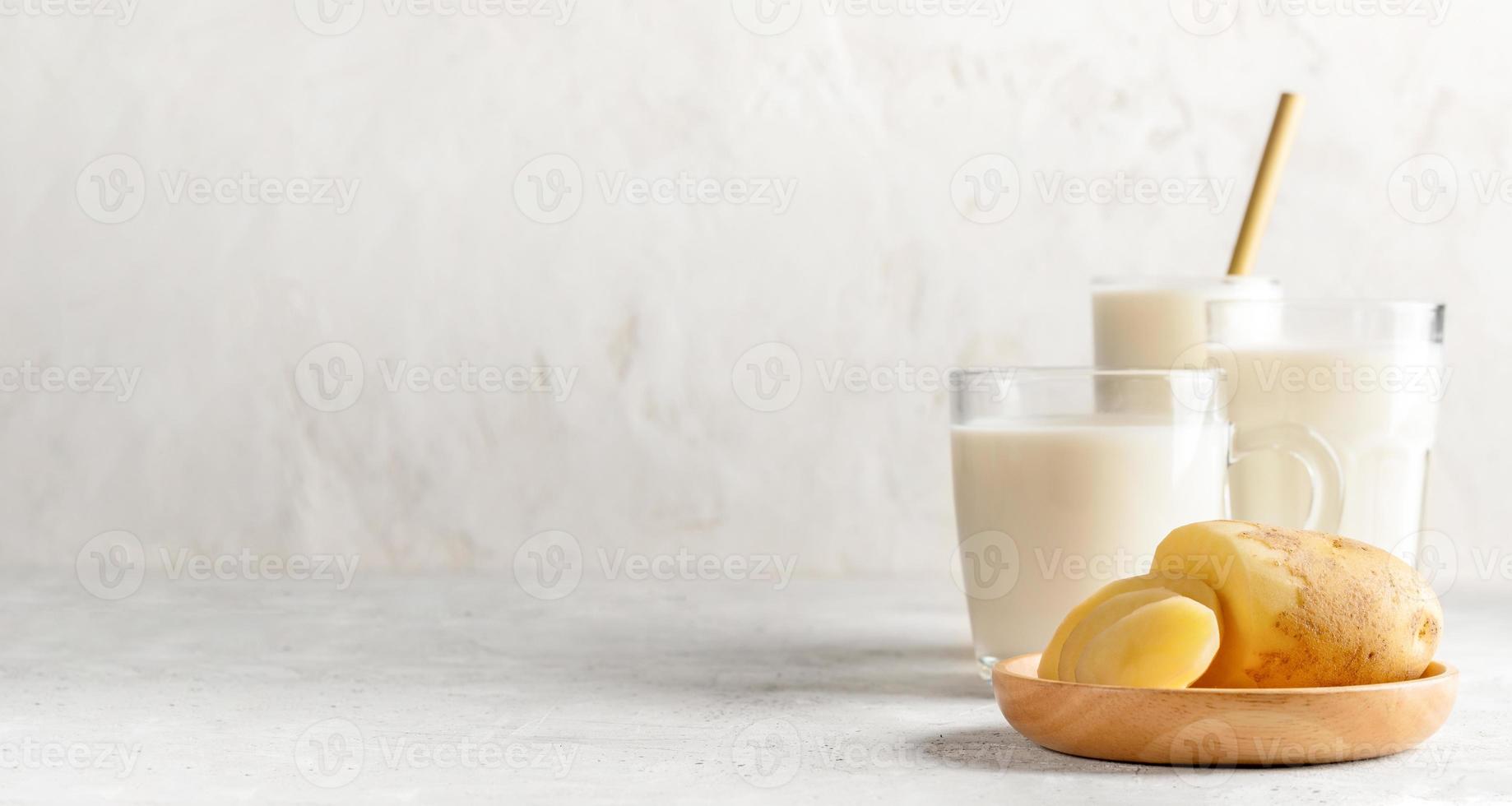 vegane kartoffelmilch in gläsern, kartoffelknolle und scheiben auf holzplatte auf neutralem hintergrund. Banner. foto