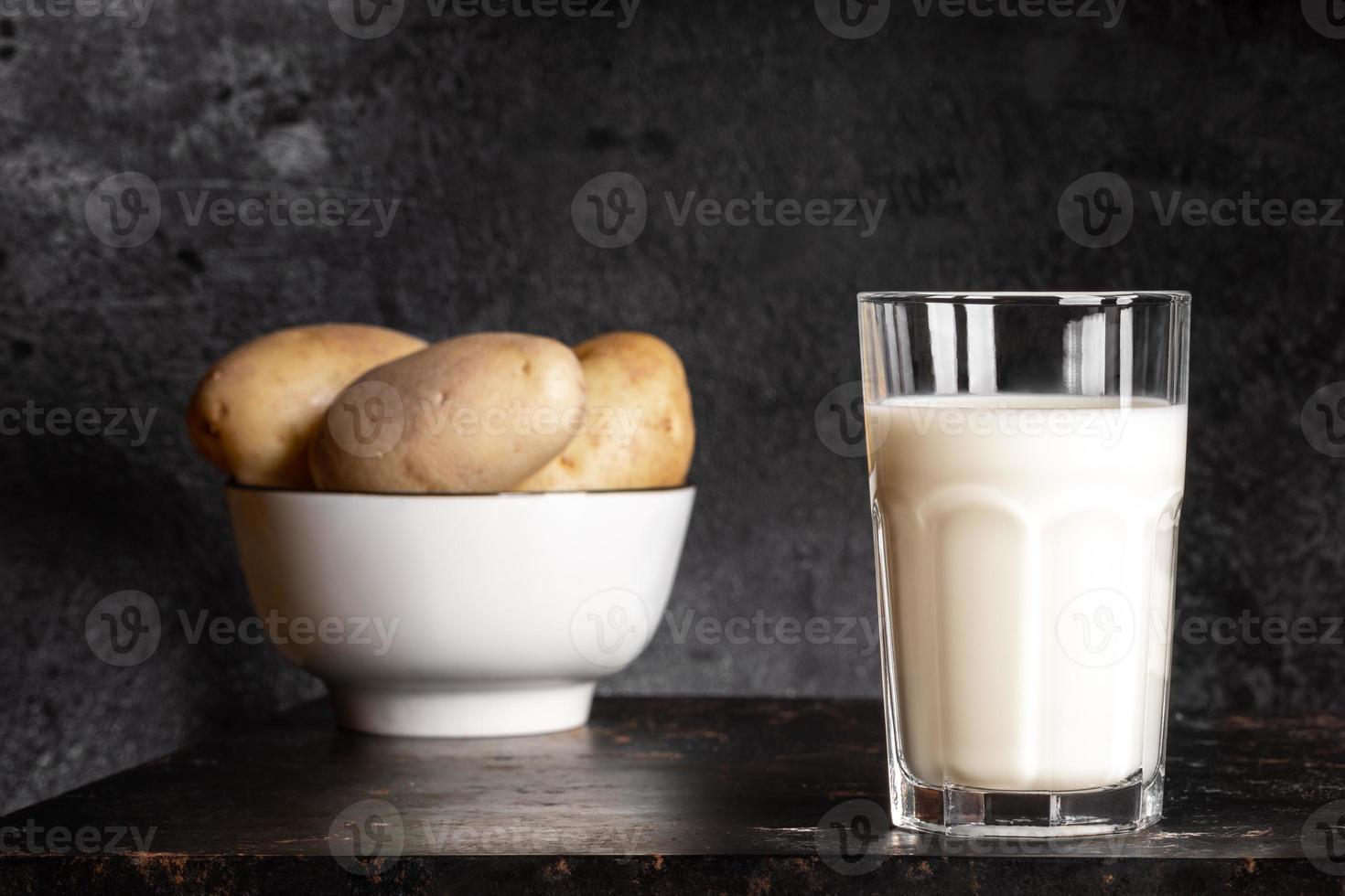 Kartoffelmilchglas und Schüssel mit Kartoffelknollen auf altem rostigem Metalltisch auf schwarzem Hintergrund. foto