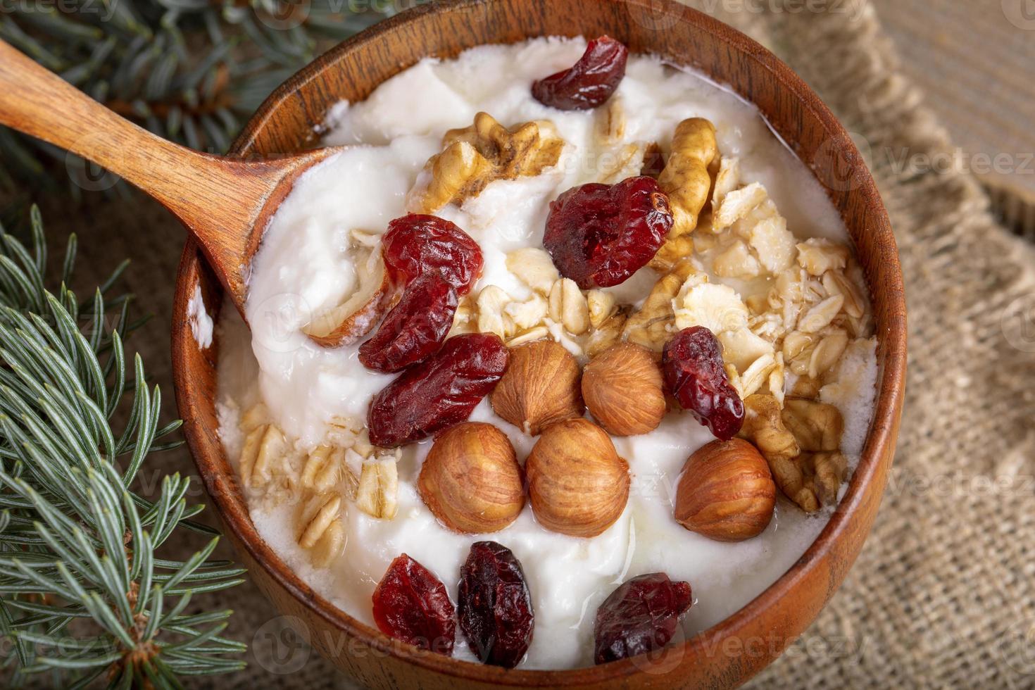 Nahaufnahme Holzschale mit Joghurt mit Haferflocken, Nüssen und getrockneten Preiselbeeren auf Sackleinen. foto