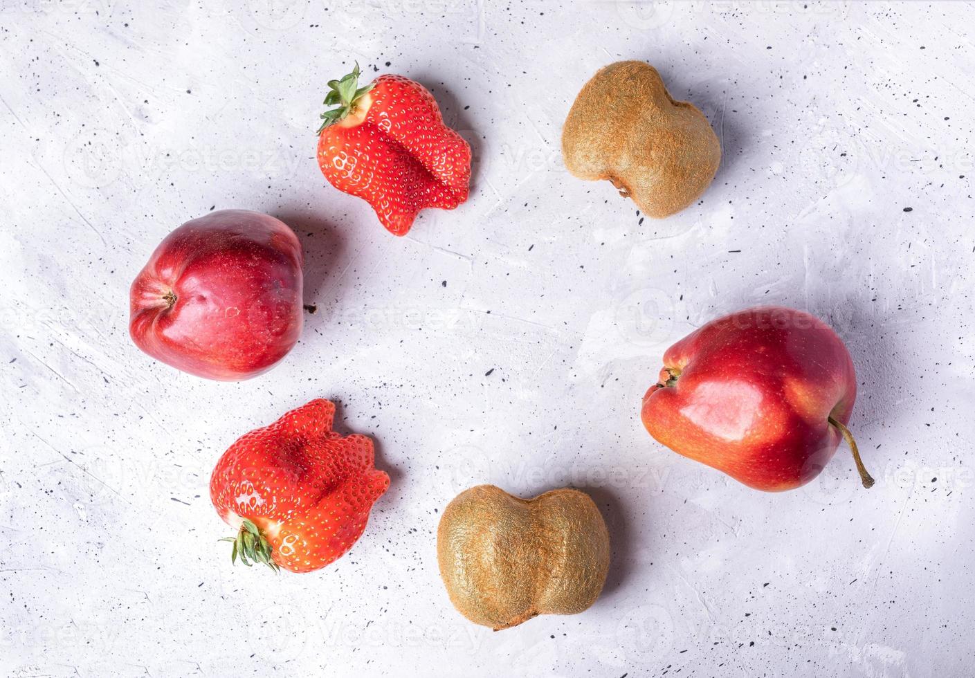 Sechs hässliche Früchte und Beeren, die im Kreis auf grauem Betongrund angeordnet sind. foto