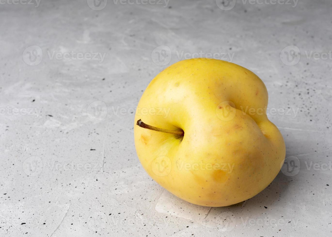 ein hässlicher gelber apfel mit einbuchtung auf grauem betonhintergrund. foto