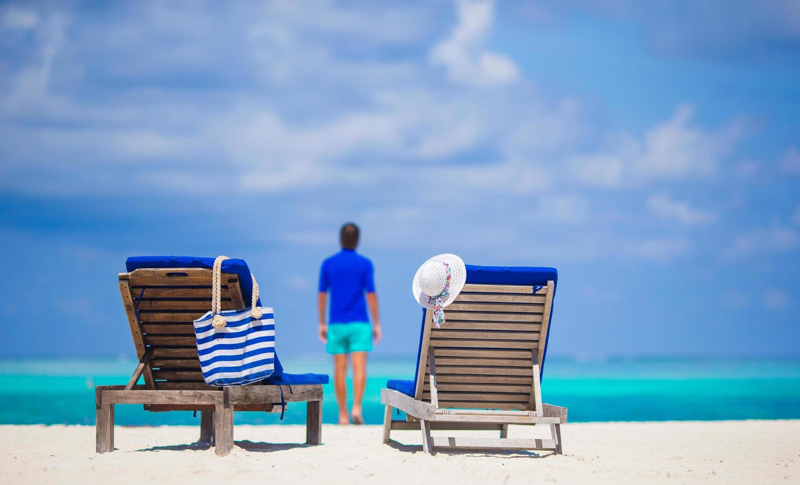 Liegestühle am Strand mit einer Person in der Ferne foto