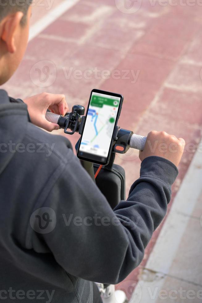 junger Mann auf einem Elektroroller mit Smartphone-GPS-Anwendungen foto