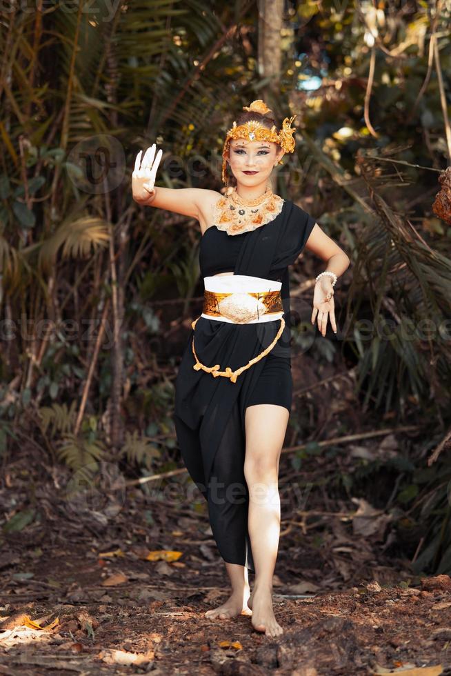 javanische Frau tanzt Pose in einem schwarzen Tanktop und schwarzem Rock mit goldener Krone und goldenen Accessoires an ihrem Körper im Dschungel foto