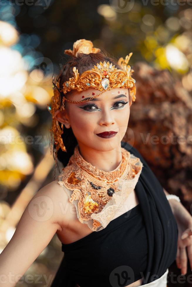 asiatische frau posiert mit ihrer hand, während sie ein schwarzes kleid und einen goldenen gürtel mit einer goldenen krone auf dem kopf trägt foto