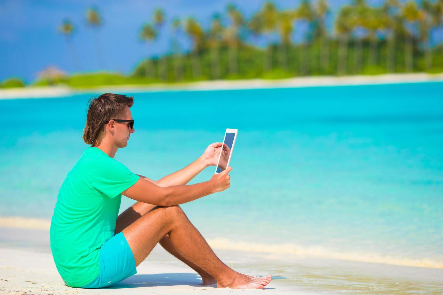 Mann mit einer Tablette an einem tropischen Strand foto