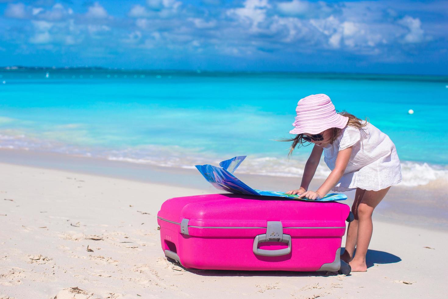 Mädchen mit rosa Koffer und einer Karte auf einem tropischen Strand foto