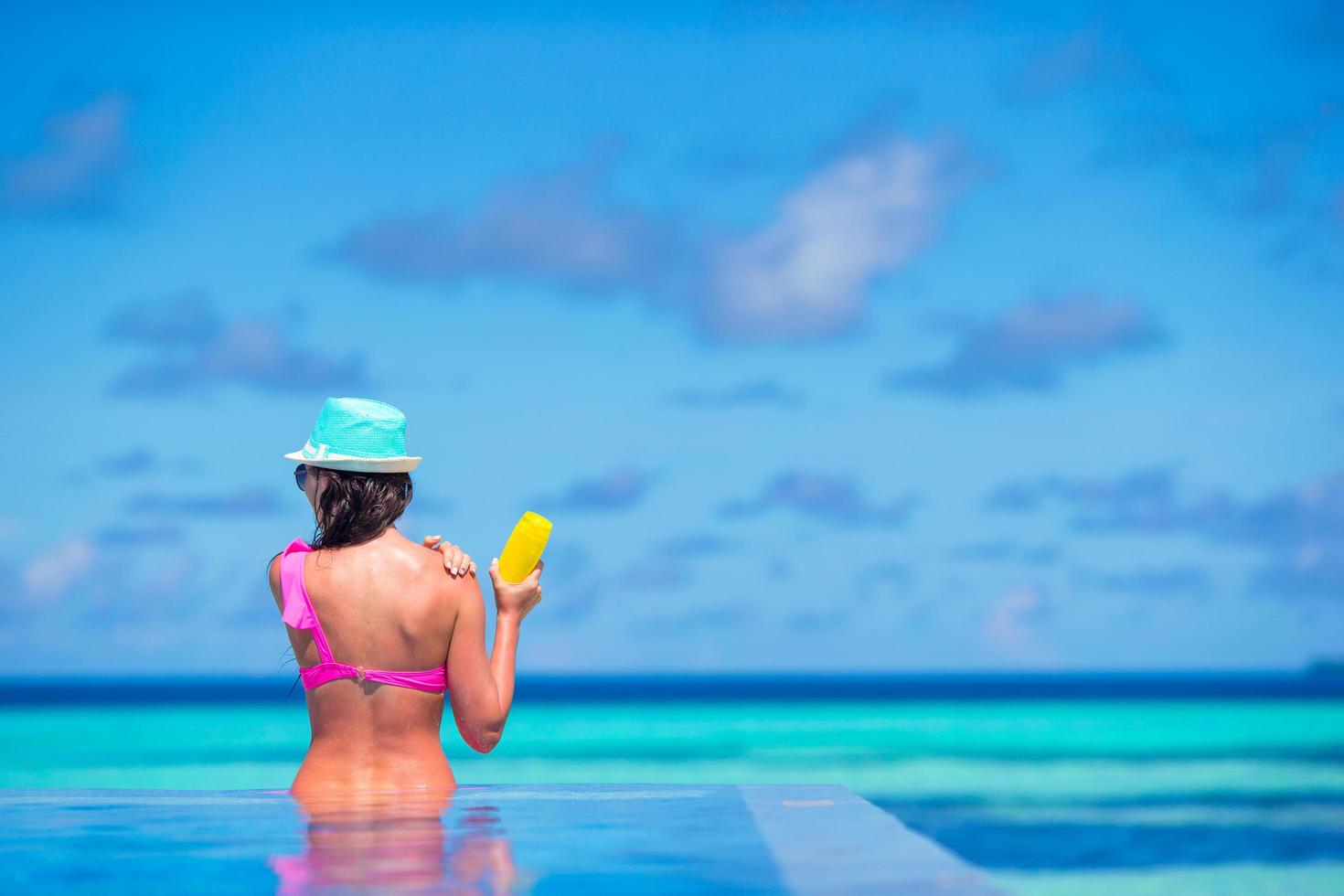 Frau, die Sonnenschutzmittel in einem Pool anwendet foto