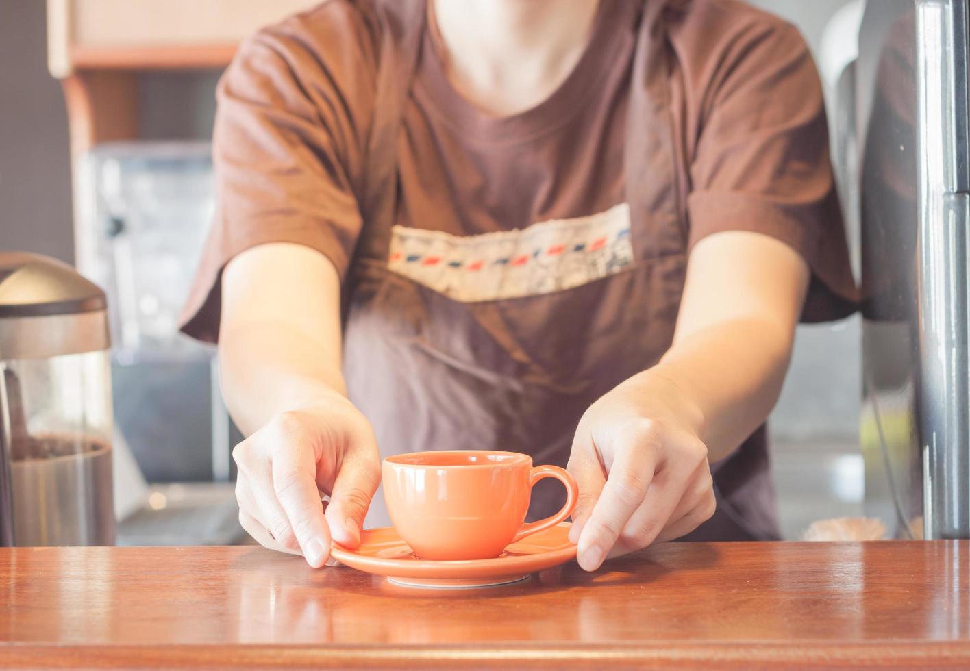 Barista bietet eine orangefarbene Kaffeetasse an foto