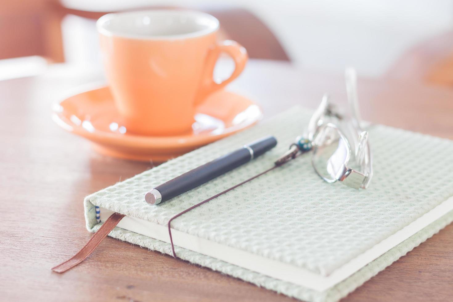 Notizbuch, Stift und Brille mit orangefarbener Kaffeetasse foto