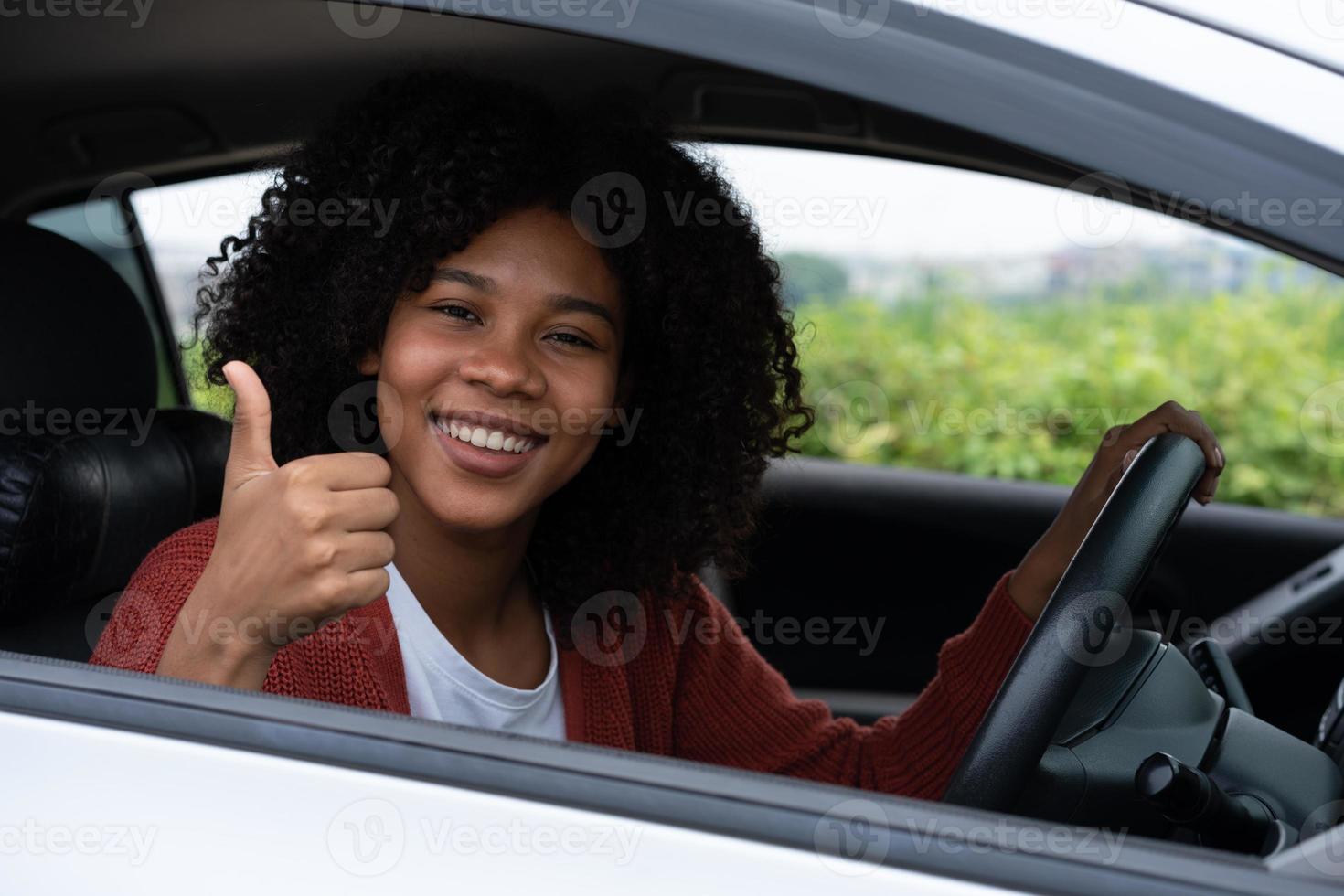 junge frau, halb asiatin, halb afrikanerin, zeigt daumen nach oben im neuen modernen auto. Aufregung der jungen Frau erster Roadtrip nach bestandener Führerscheinprüfung. Fühlt sich gut an, nachdem man ein neues Auto bekommen hat. foto