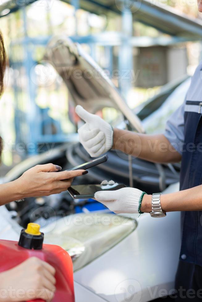 asiatische frauen erhalten kontaktnummern von automechanikern, nachdem sie das problem mit dem automotor behoben haben, und scannen den qr-code, um für das tanken zu bezahlen, nachdem ihnen auf der straße der treibstoff ausgegangen ist. autoreparatur- und wartungskonzept. foto