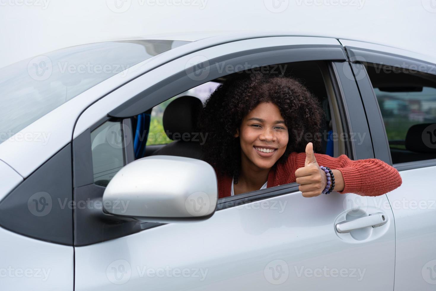junge frau, halb asiatin, halb afrikanerin, zeigt daumen nach oben im neuen modernen auto. Aufregung der jungen Frau erster Roadtrip nach bestandener Führerscheinprüfung. Fühlt sich gut an, nachdem man ein neues Auto bekommen hat. foto