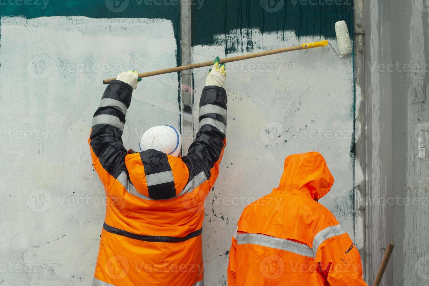 Arbeiter malen Wand. Wandpeitschen. orange Kleidung der Arbeiter. schmierende Graffiti. foto