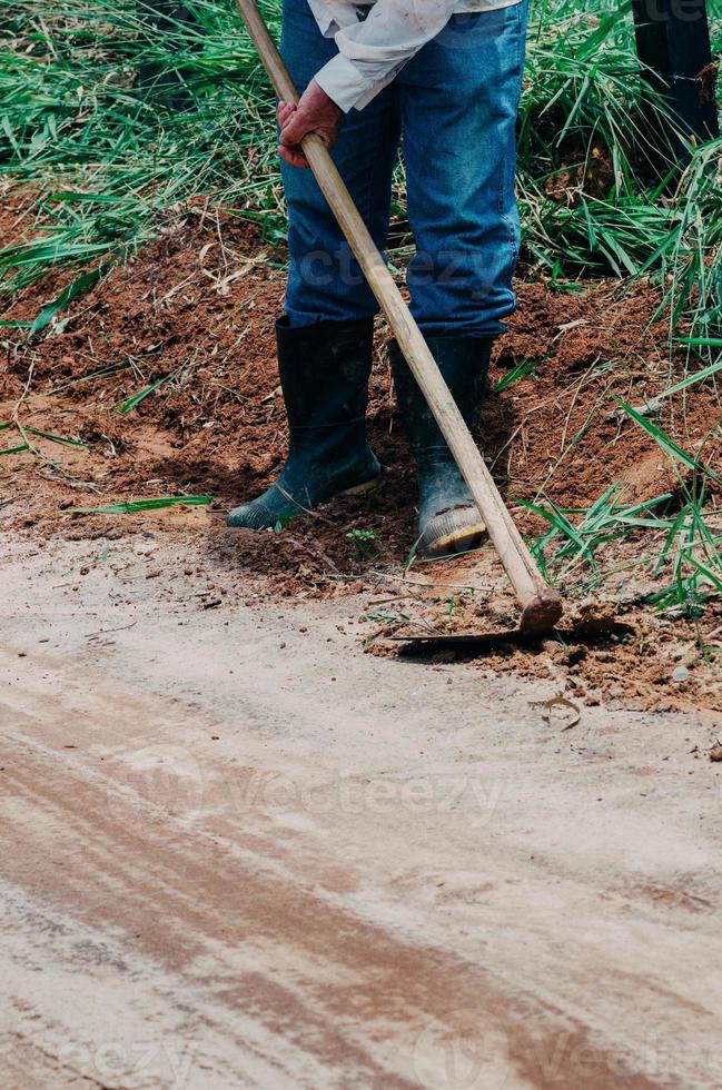 Nicht identifizierbarer Landarbeiter, der Unkraut mit einer Hacke in einem Bauernhof schneidet foto