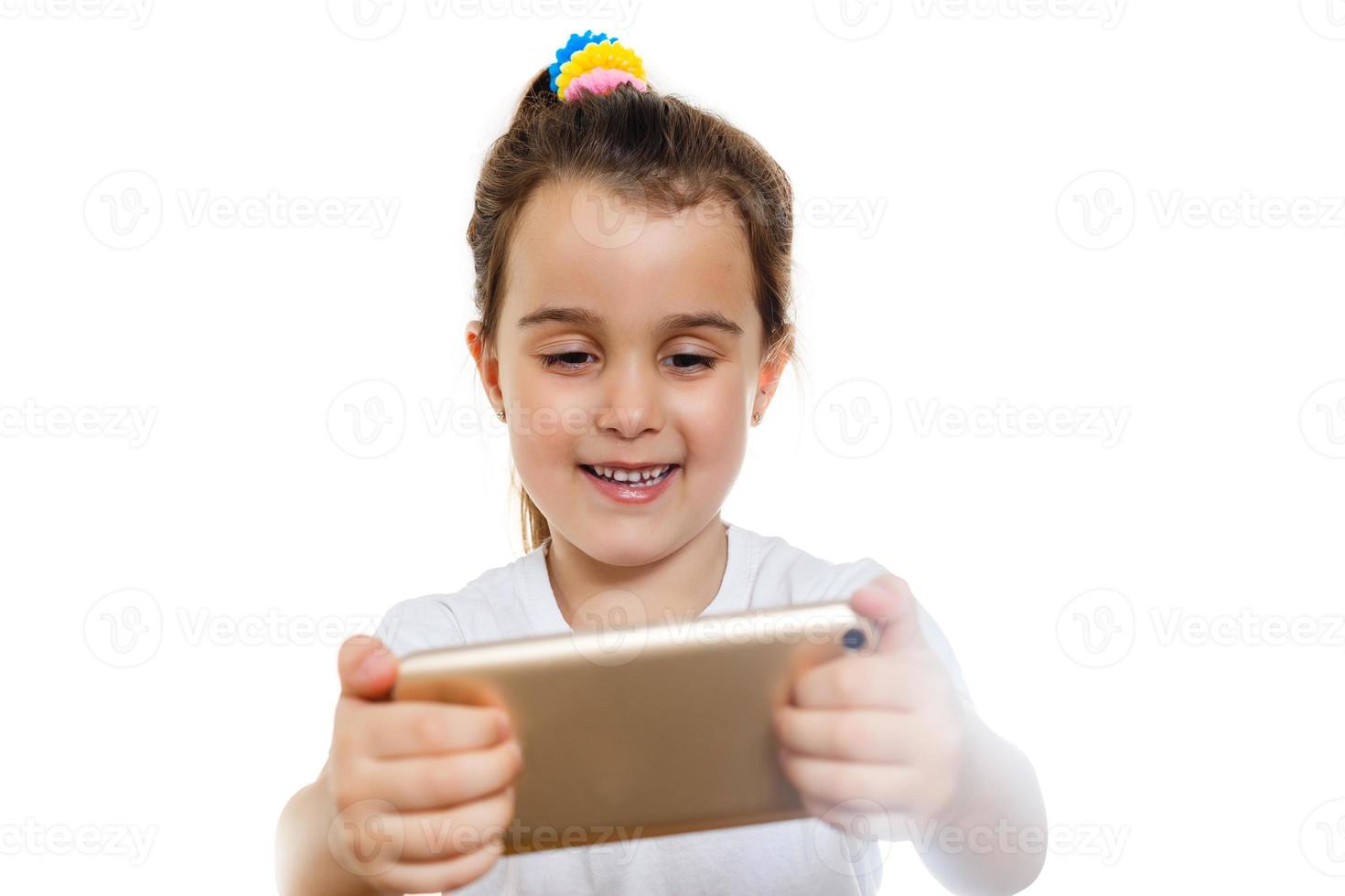 Kleines Mädchen schaut den Cartoon auf dem Handy im Hintergrundkonzept der weißen Wand foto