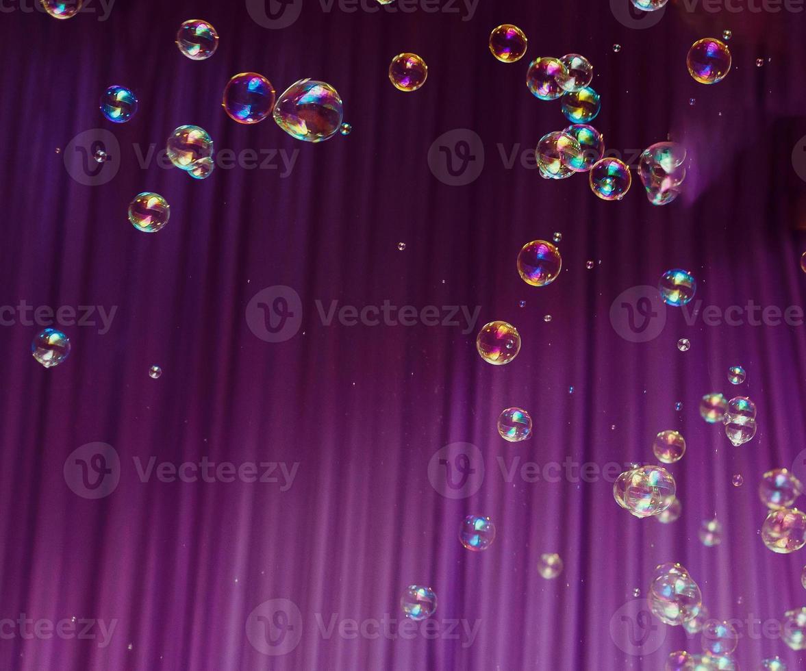 Wasser lässt Seifenblasen auf buntem purpurrotem Hintergrund fallen foto
