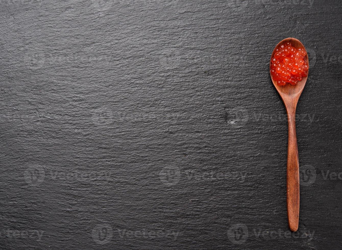frisch gekörnter roter Lachskaviar in Holzlöffel, schwarzer Hintergrund, Draufsicht foto